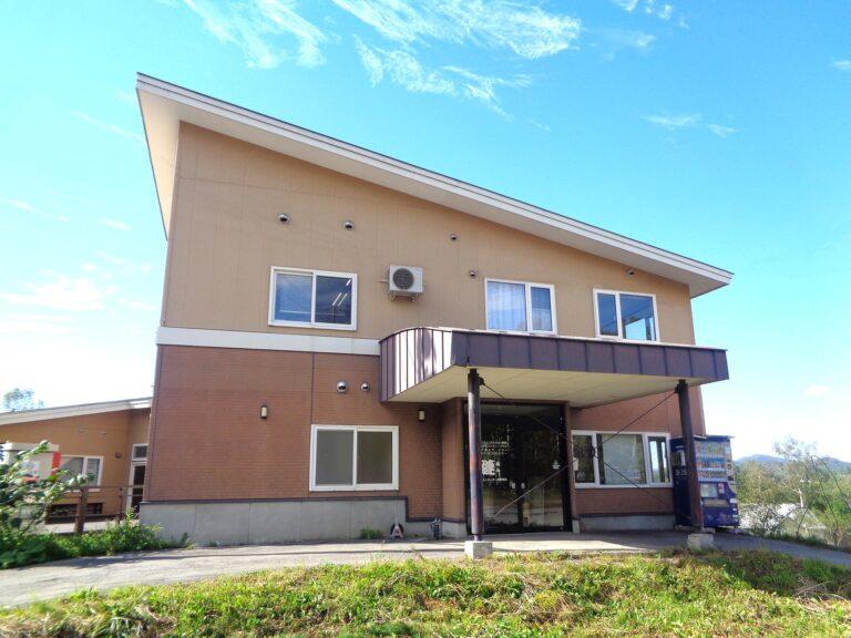 介護施設の建物外観。茶色いレンガ造りで、バルコニーと駐車スペースを備えた2階建て。